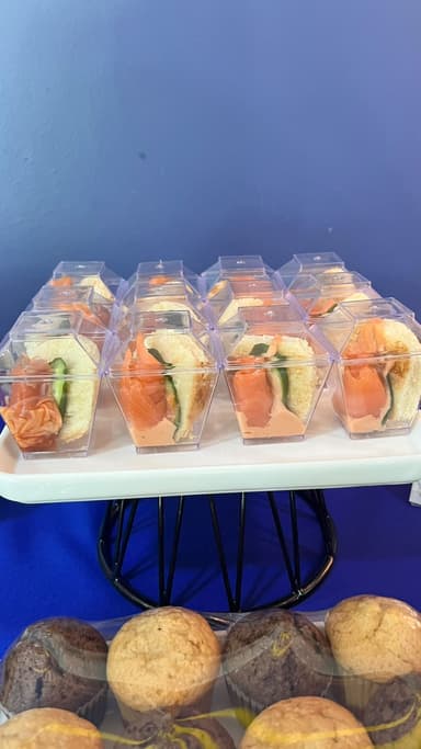 Salmon sandwiches on a stand above a tray of muffins
